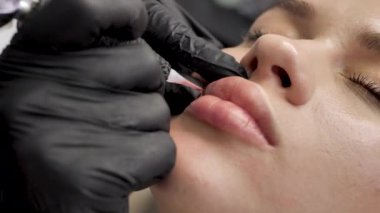 Bir kozmetolog güzellik salonundaki dudaklara kalıcı makyaj uygular. Dövme