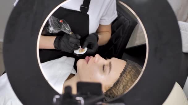 En kosmetolog applicerar permanent makeup på läpparna i en skönhetssalong. Tatuering — Stockvideo