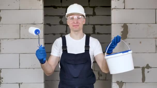 Jovem trabalhador da construção masculina com uma escova e balde isolisolado em uma parede de tijolo — Vídeo de Stock