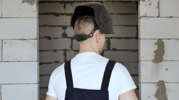 青い手袋の男の建設労働者はレンガの壁に溶接マスクを置きます — ストック動画