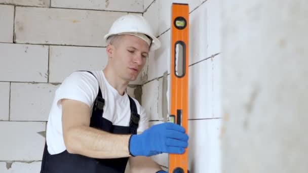 Mooie jonge architect of bouwer in een witte harde hoed controleert het niveau van de muur met de level tool — Stockvideo