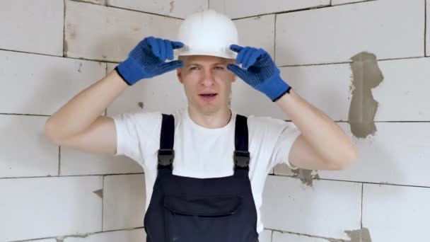 En manlig byggarbetare i vit hjälm gäspar på en byggarbetsplats — Stockvideo