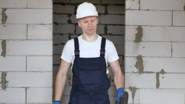 Elinde matkapla kasklı bir erkek inşaat işçisi inşaat alanında eğleniyor.