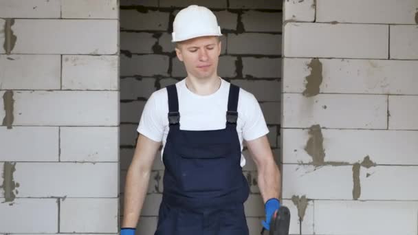 A male construction worker in a helmet with a drill in his hands is messing around and having fun at a construction site — Stock Video
