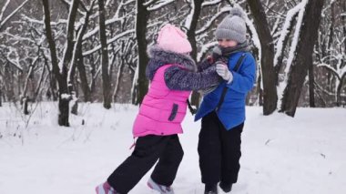 Çocuklar kışın ormanda oynarlar, bir kız çocuğu kar yığınına iter. Yavaş çekim.