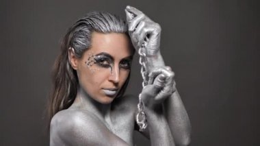 Güzel bir kadın, cildinde gümüş boya, saçlarında da zincir var.