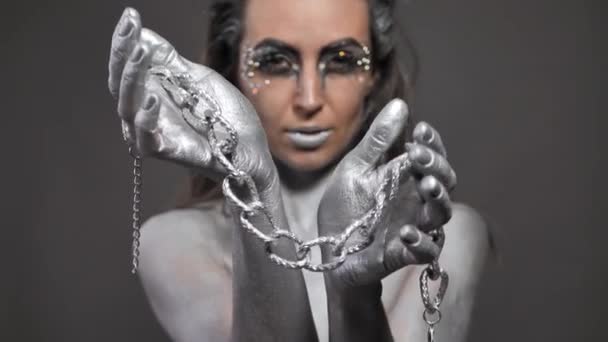 Schöne Frau mit Silberfarbe auf der Haut und Haaren spielt mit einer Kette in ihren Händen — Stockvideo
