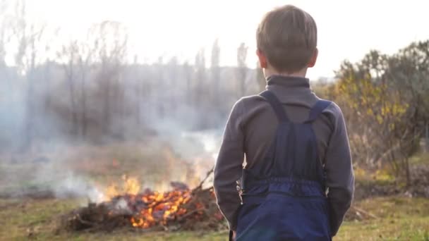 Силуэт ребенка на фоне костра осенью. Опасность пожара на открытом воздухе — стоковое видео