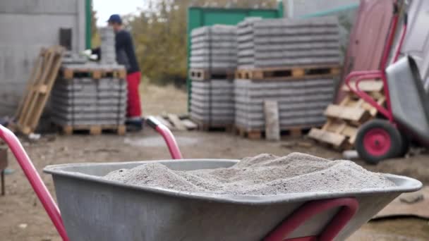 Carretilla de construcción con cemento y una pala en el fondo de una pila de baldosas grises — Vídeos de Stock