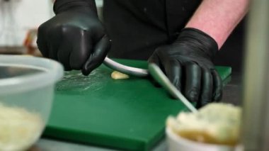 Şef tahtanın üzerinde sarımsak öğütüyor.