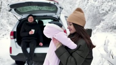 Genç anne küçük kızını kollarına aldı ve onu sardı. Kışın karla kaplı ormanda aile eğlencesi