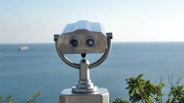 Deniz kıyısında halka açık dürbünler, yakın çekim. Gün batımı ve denizin bulanık arka planında bozuk para dürbünü görüntüleyici