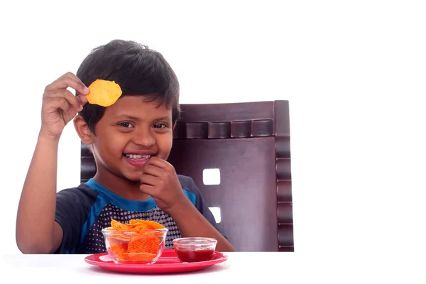 Happy & smiling Indian boy eating unhealthy chips. The kid is sc — Stock Photo, Image