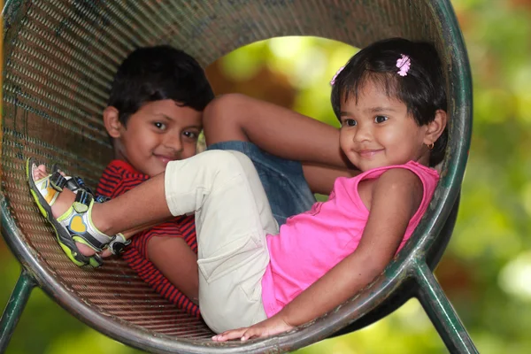 Lindos niños pequeños (niño y niña) jugando en el túnel en el patio de recreo —  Fotos de Stock