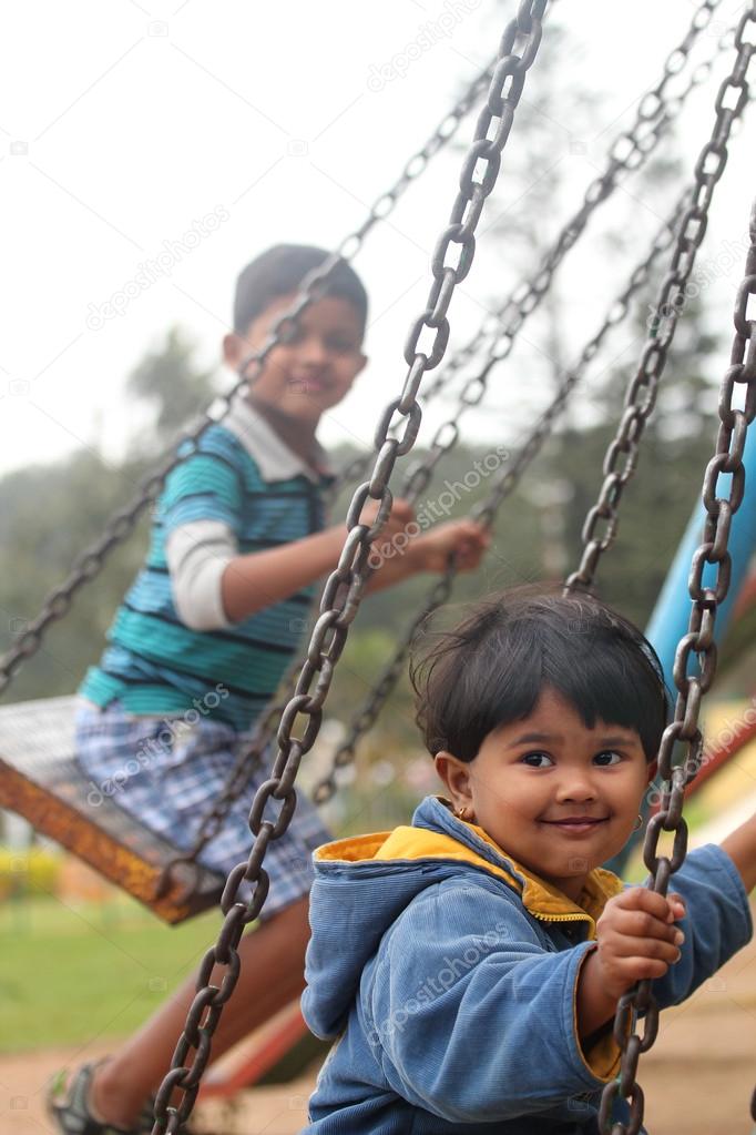 Cute young happy kids playing on swing sets in a park