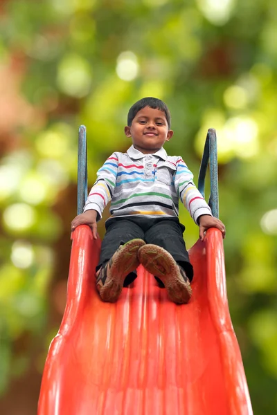 Muito sorridente indiana menino (criança) no controle deslizante em um parque — Fotografia de Stock