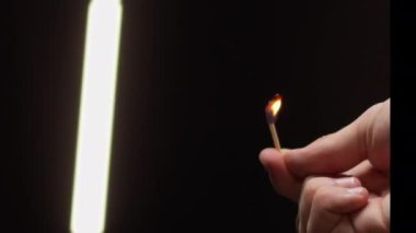 Erkek parmakları yanan kibriti tutar, karanlık stüdyoyu aydınlatır.