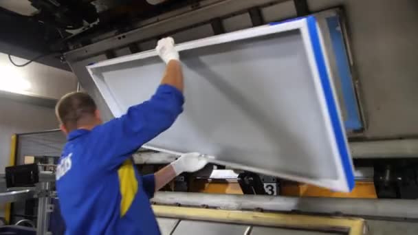 Employee in uniform puts detail of fridge onto machine — Stock Video