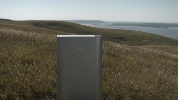 Металеві холодильники стоять на дикій луці на горбистому березі. — стокове відео