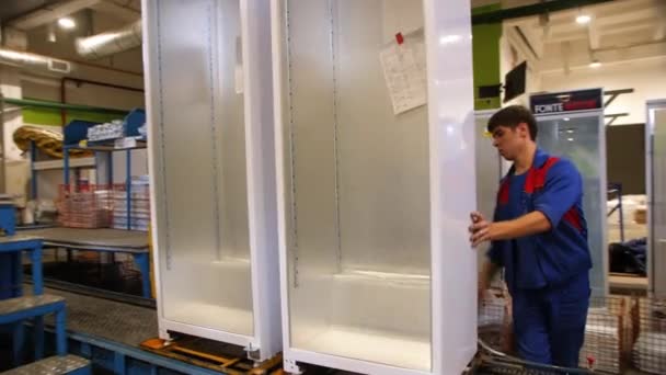 Молодий працівник налаштовує корпус холодильника на конвеєрі. — стокове відео