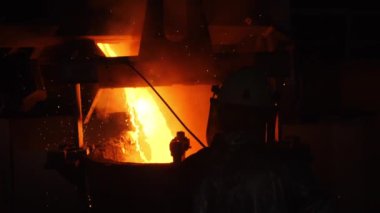 İşçi, karanlık atölyede sıcak sıvı metal dökmeye bakıyor