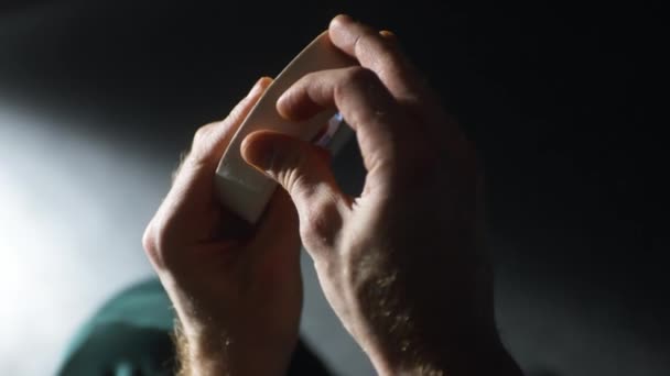 Homme ramasse bord de plâtre médical blanc dans une pièce semi-sombre — Video