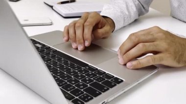 Dizüstü bilgisayarı olan bir adam beyaz masada oturuyor.
