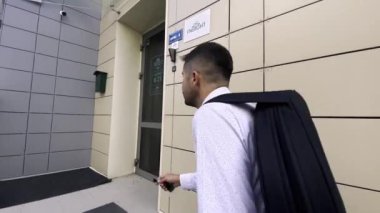 Siyah çantalı tef taşıyan bir adam bina girişine geliyor.