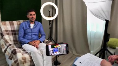 Adam sunucuyla konuşuyor ve şık bir stüdyoda röportaj veriyor.