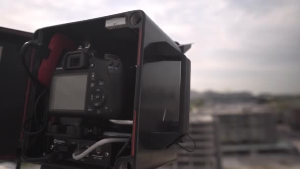 Camera in casing on building roof to shoot construction site — Stock Video