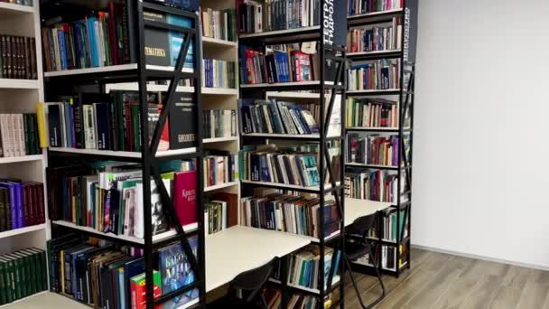 Mesas vacías cerca de estantes con diferentes libros en la biblioteca — Vídeo de stock