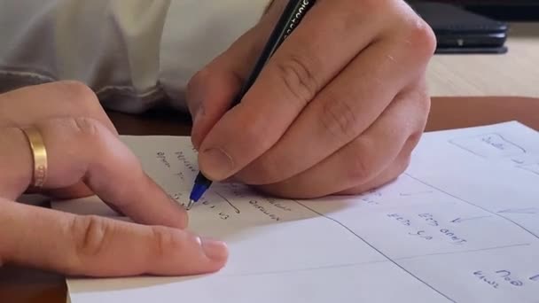 Manager writes in table cell of schedule at wooden desk — Stock Video