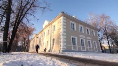 Adam karlı caddede köpeğini gezdiriyor. Eski binaları geçiyor.