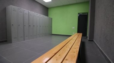 Boş soyunma odası, ahşap bank ve sıra sıra gri dolaplar.