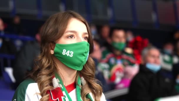 Молодая женщина в зеленой маске смотрит хоккей на арене — стоковое видео