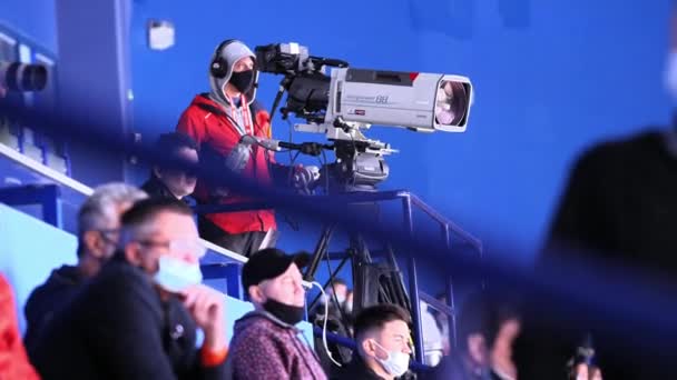 Cameraman com máscara e fone de ouvido dispara jogo de hóquei em stand — Vídeo de Stock