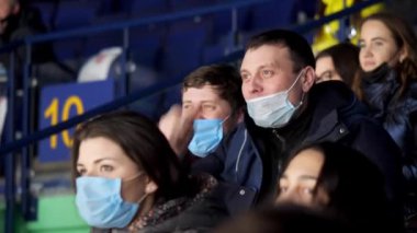 Maskeli olumlu bir adam hokey maçında arkadaşıyla konuşur.