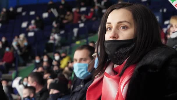 Любительница спорта с маской смотрит хоккей на стадионе — стоковое видео