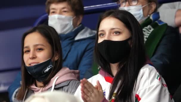 Hübsche Sportfans mit medizinischen Masken schauen sich Eishockeyspiel an — Stockvideo