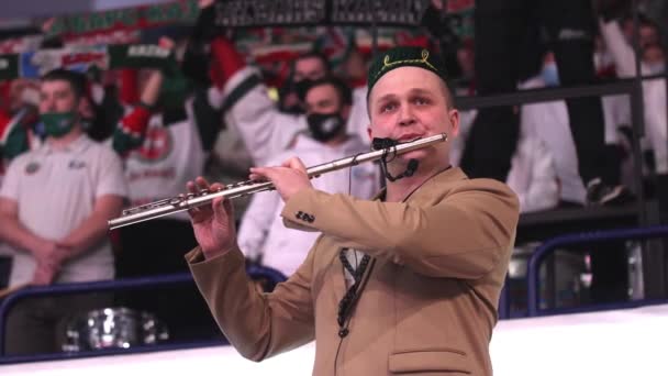Музыкант на тубетейке играет на флейте, выступая на хоккейном матче — стоковое видео