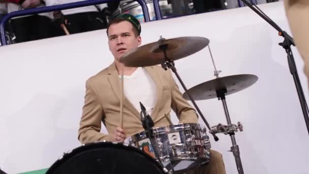 Νεαρός μουσικός σε μπεζ κοστούμι παίζει τύμπανα με μπάντα στο χόκεϊ — Αρχείο Βίντεο