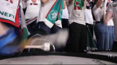Erkekler davul çalar ve taraftarlar buz pistinde hokey takımını destekler