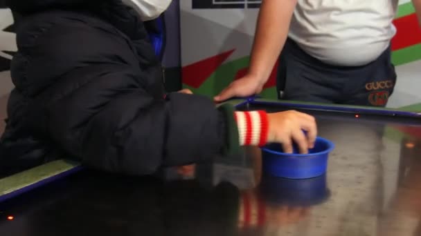 Маленька дитина в масці і теплий піджак грає в аерохокей в залі — стокове відео