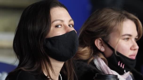 Jonge vrouw met masker en vriend kijken spel van hockey team — Stockvideo