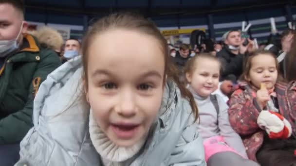 Little girl looks in camera watching hockey with family — Stock Video