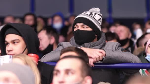Man met masker en warme hoed leunt op leuning kijken hockey — Stockvideo