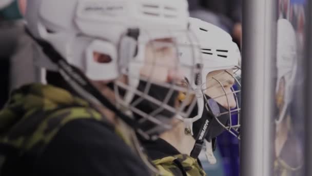 Młodzi fani sportu w kaskach hokejowych oglądają turniej na lodowisku — Wideo stockowe