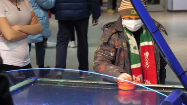 Kind met masker in warme kleren speelt air hockey in het centrum — Stockvideo