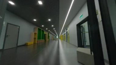 Yeni okul binasının ahşap rafları ve boş merdivenlere açılan kapıları olan geniş bir koridor.
