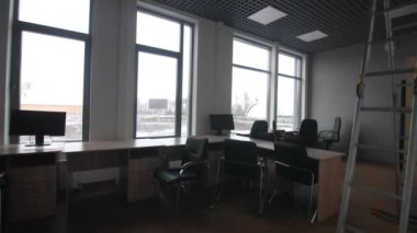 Rahat sandalyeli ahşap masalar ve tamir edilmiş ofisin geniş pencerelerinin yanında katlanmış merdivenli modern bilgisayarlar.